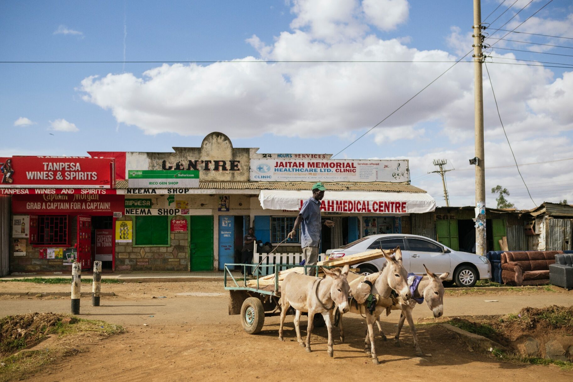 A man leads a team of donkeys past a roadside row of shops in rural Kenya