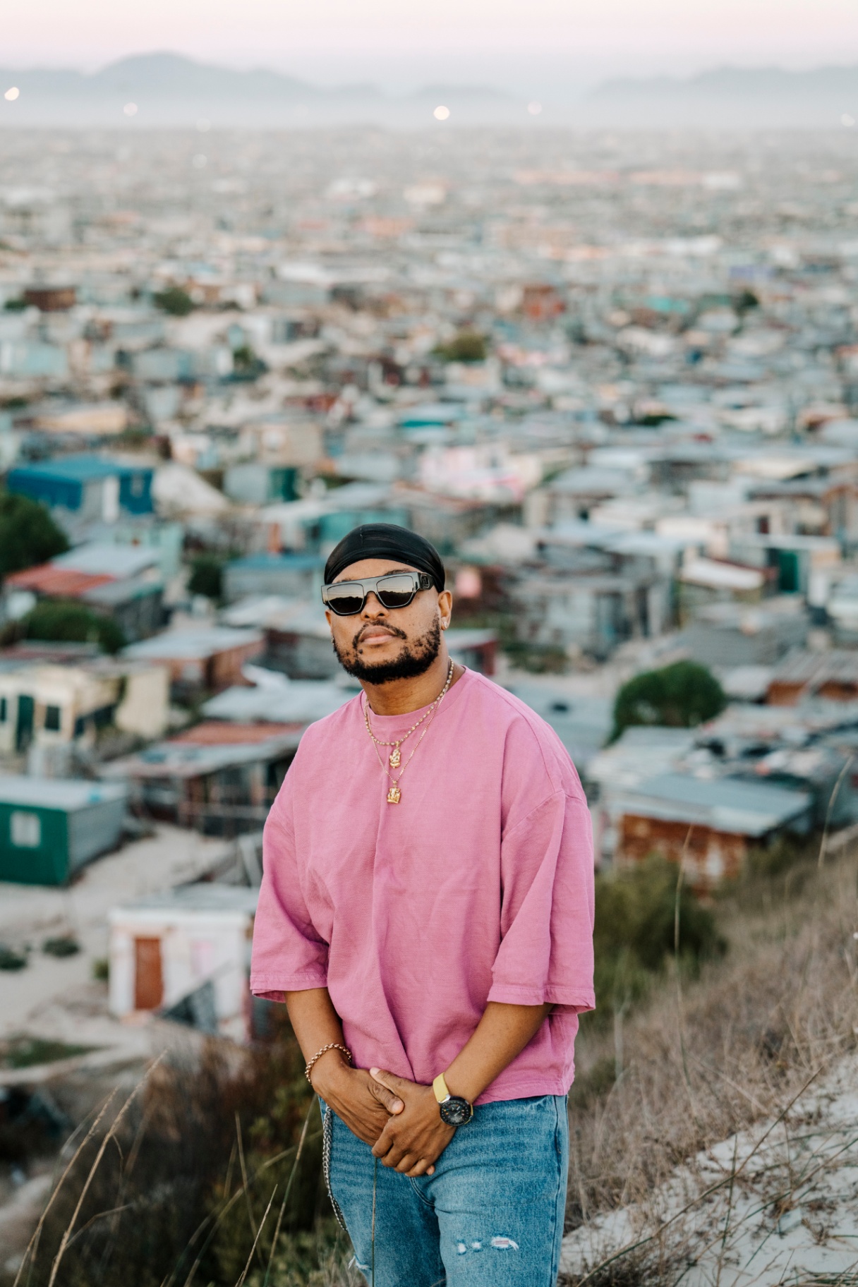 KO standing on a hillside above a vast Cape Town informal settlement at dusk