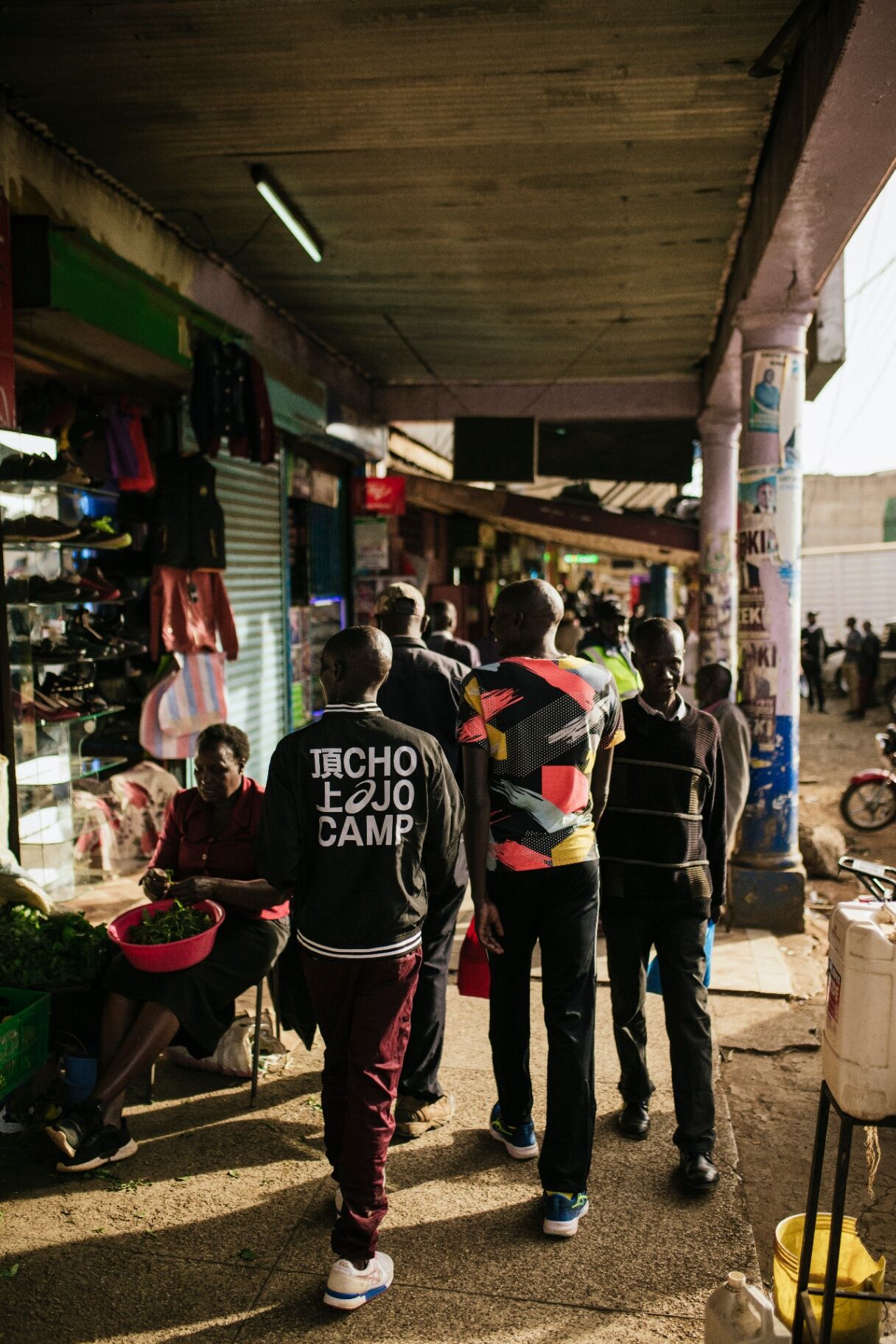 Athlete walking through a market wearing a 頂上 CHOJO CAMP bomber jacket