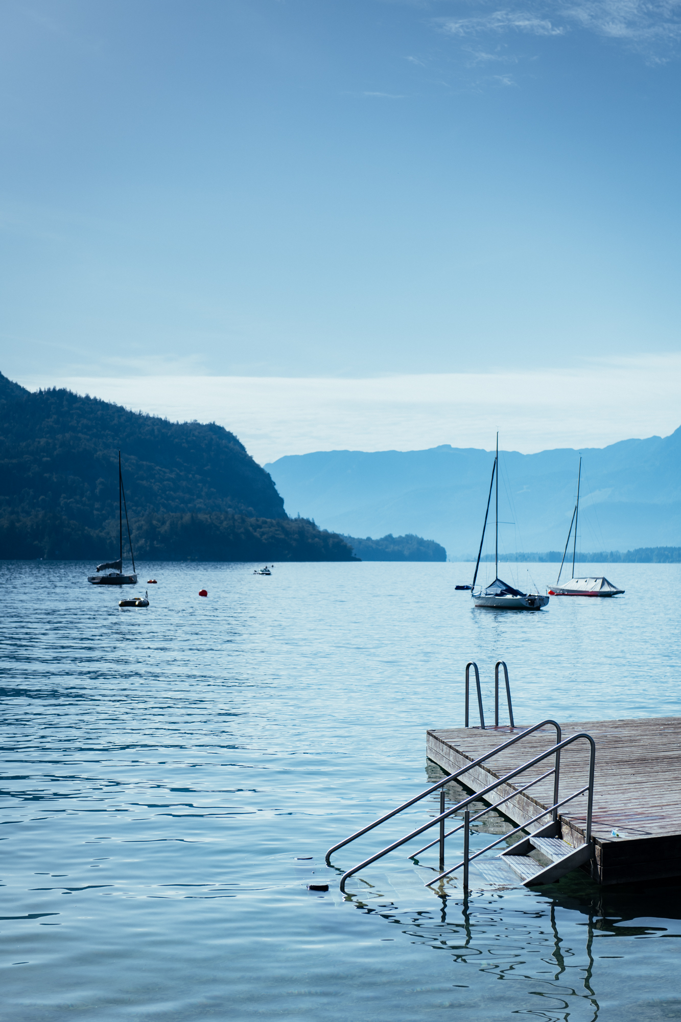 Mirror-calm Wolfgangsee at dawn with sailboats and a wooden swimming dock