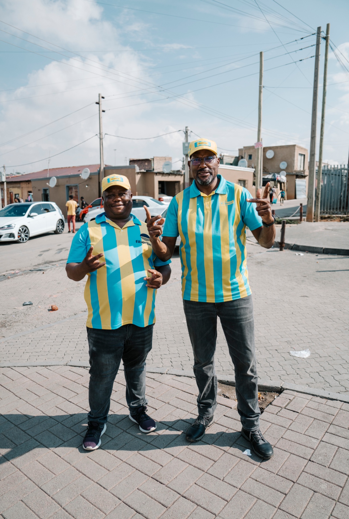 Two Fibertime ambassadors in branded stripe shirts on a township street corner