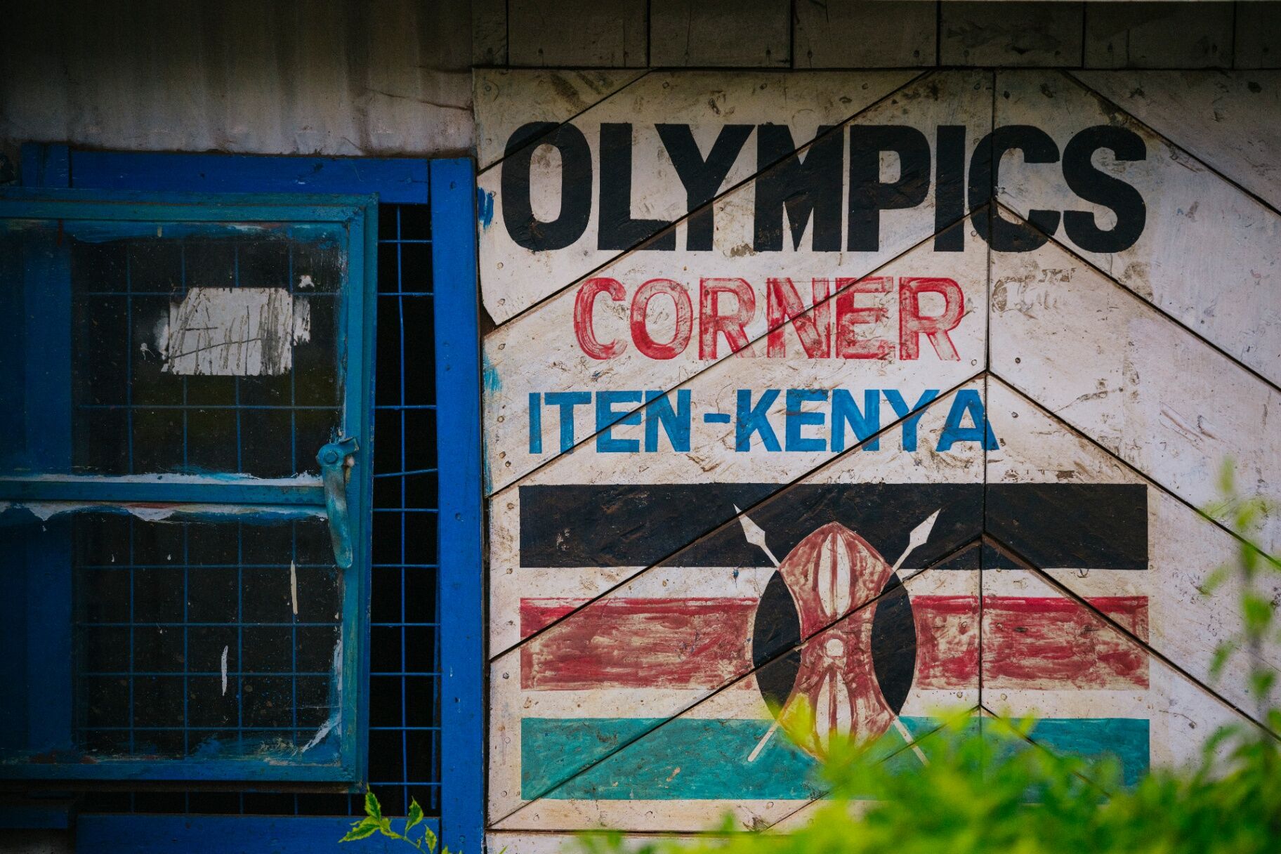 Hand-painted 'Olympics Corner Iten — Kenya' sign on a weathered wooden wall